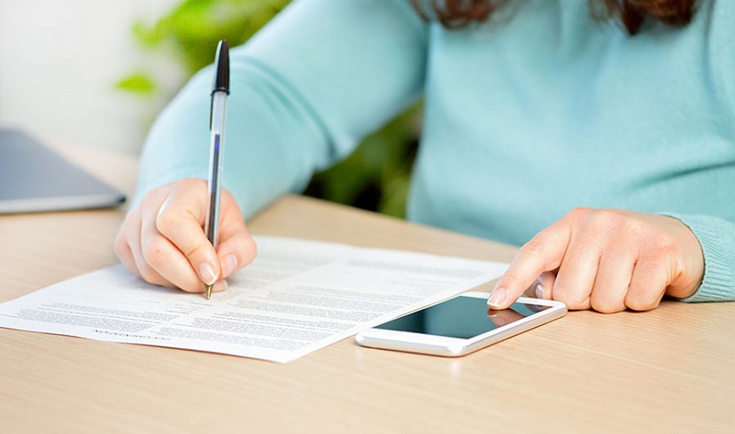 dwylo rywun yn llenwi ffurflen ac ar y ffôn