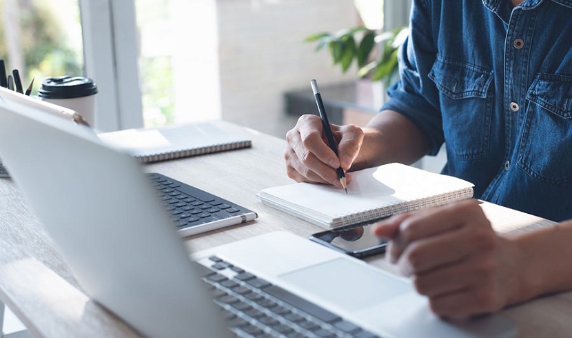 person ar gliniadur, ac hefyd yn sgwennu ar bapur